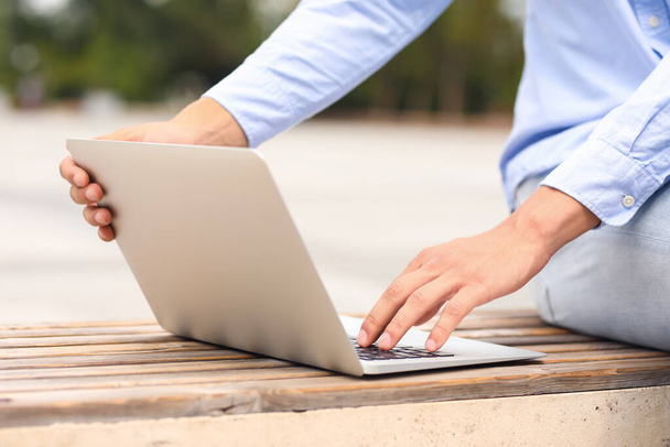 Young man using laptop on bench outdoors, closeup - Foto, imagen