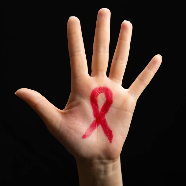 A female hand reaches up with a red awareness ribbon drawn on the palm. Black background. World AIDS day concept. - Photo, Image