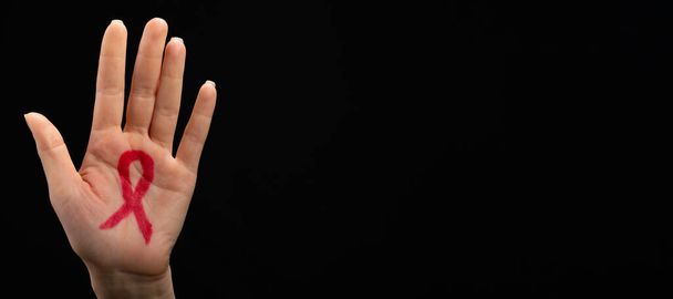 Una mano femenina alcanza con una cinta roja dibujada en la palma de la mano. Fondo negro. Concepto del Día Mundial del SIDA. - Foto, imagen
