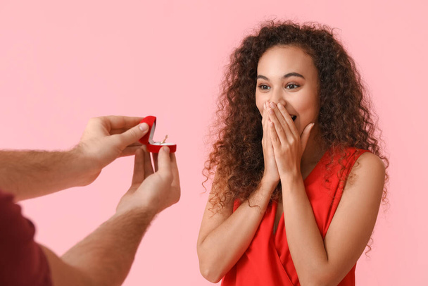 Young man proposing to his surprised girlfriend on color background - 写真・画像