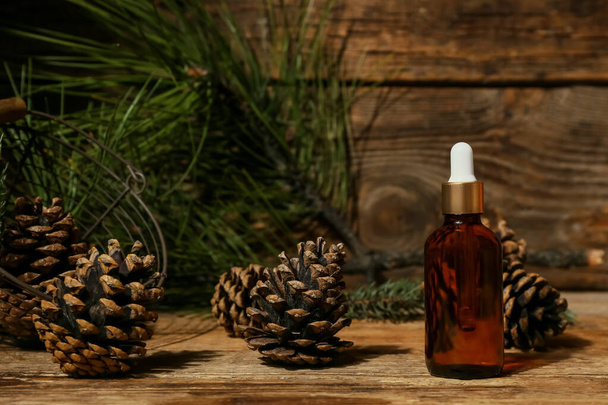 Bottle of essential oil, pine cones and branch on wooden background - Фото, изображение