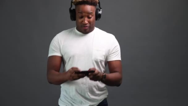 Enthusiastic African man with headphones is playing a game on a smartphone - Metraje, vídeo
