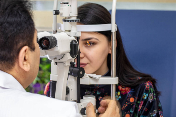 Αρσενικός γιατρός οφθαλμίατρος ελέγχει την όραση των ματιών της όμορφης νεαρής γυναίκας στη σύγχρονη κλινική. Γιατρός και ασθενής στην οφθαλμολογική κλινική. - Φωτογραφία, εικόνα