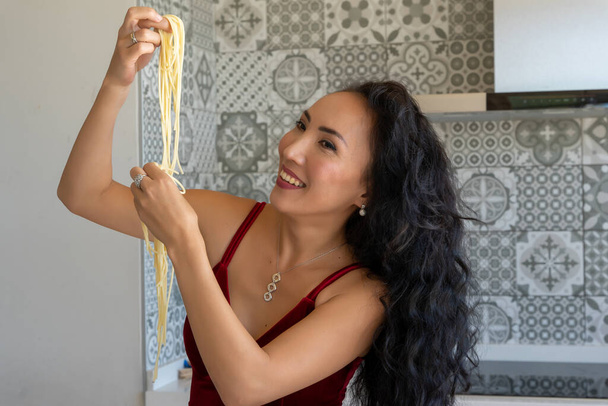 glimlachende vrouw houden pasta omhoog en kijken naar het, horizontale achtergrond met patroon tegels - Foto, afbeelding