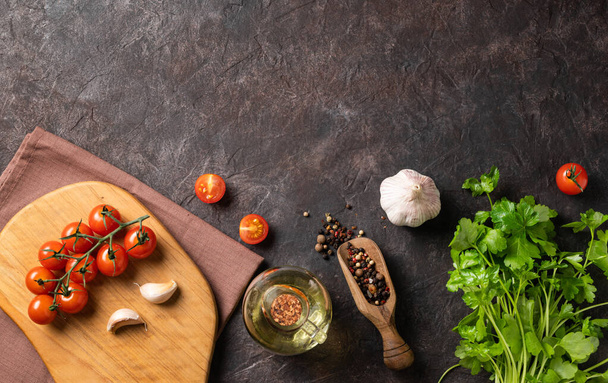 Specerijen en verse kruiden peterselie, knoflook, peper, tomaten en olie op een donkerbruine achtergrond. Het concept van lekker en gezond eten. Bovenaanzicht en kopieerruimte. - Foto, afbeelding
