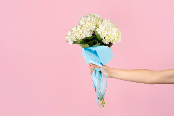 Hand holds a bouquet of beautiful tender white hydrangea on light pink background. Flowers as gift for teacher or mother day, international womens day or Valentines day. Banner with copy space - Photo, Image