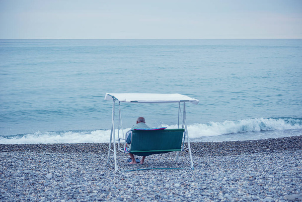 Elderly man sits in the chair by the sea. - Foto, afbeelding