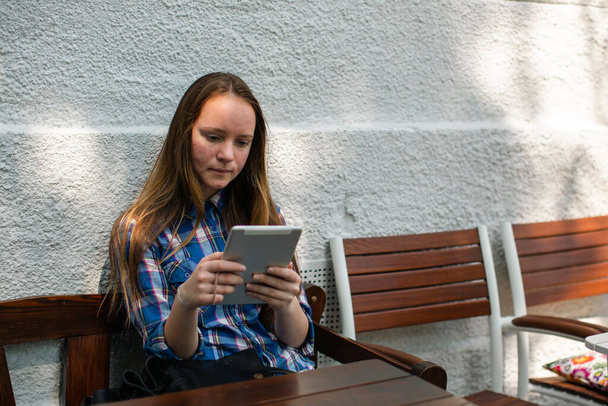 A teengirl sits with a tablet in an outdoor cafe. - Photo, Image