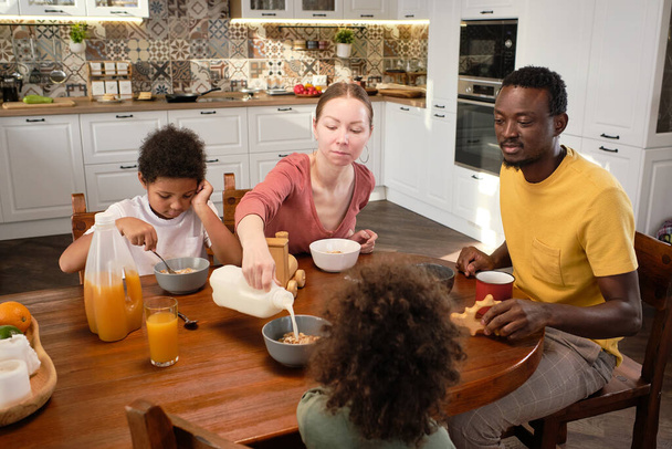 Молодая межрасовая семья отца, матери и двух милых сыновей завтракают - Фото, изображение