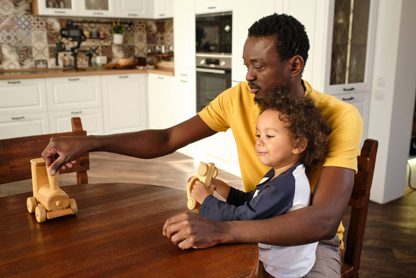 Νεαρός Αφρικανός με καθημερινά ρούχα παίζει με τον χαριτωμένο γιο του. - Φωτογραφία, εικόνα