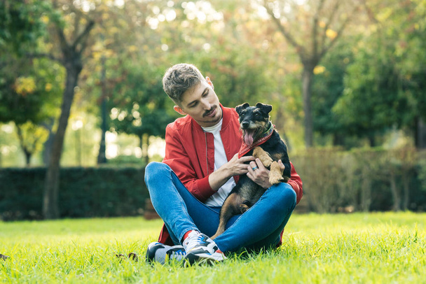 Un homme assis sur l'herbe caressant un chien dans un parc - Photo, image