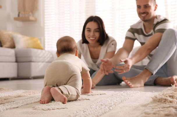 Happy parents watching their cute baby crawl on floor at home - Foto, afbeelding