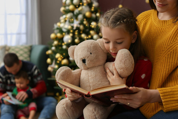 Mother with her cute daughter reading book in room decorated for Christmas - Foto, imagen