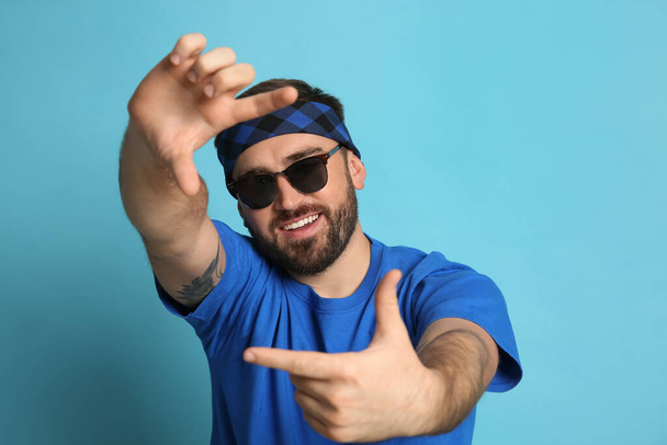 Fashionable young man in stylish outfit with bandana on light blue background - Фото, зображення