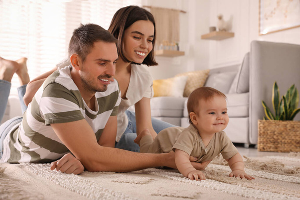 Happy parents helping their cute baby to crawl on floor at home - Photo, image