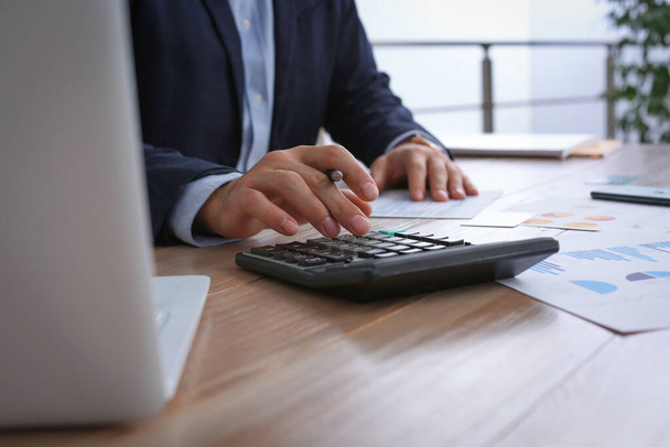 Налоговый бухгалтер с калькулятором работает за столом в офисе, крупным планом - Фото, изображение