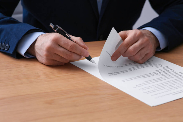 Businessman signing contract at wooden table, closeup of hands - Fotó, kép