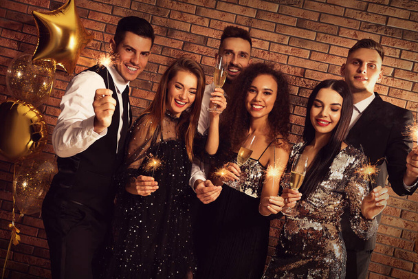 Happy friends with glasses of sparkling wine and sparklers celebrating New Year indoors - Zdjęcie, obraz