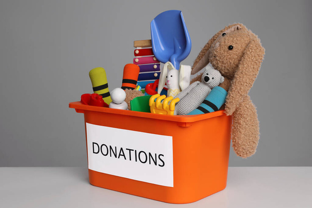 Donation box with different toys on white table against grey background - Foto, afbeelding