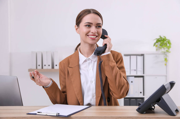 Female receptionist with clipboard talking on phone at workplace - Zdjęcie, obraz
