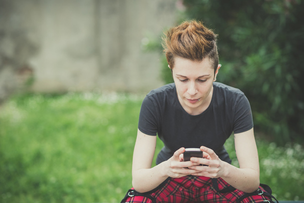 молода лесбіянка стильний стиль волосся жінка використовує смартфон
 - Фото, зображення