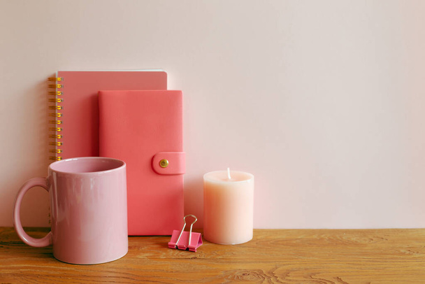 Pink notebook, mug cup, candle on wooden desk. workspace - Foto, imagen