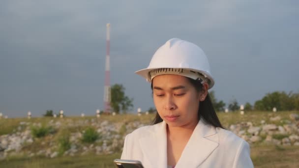 ダム建設現場でスマートフォンを操作して発電を行う女性エンジニア。ダム建設現場を見て白いヘルメットに自信の女性建築家。クリーンエネルギーとテクノロジーの概念. - 映像、動画
