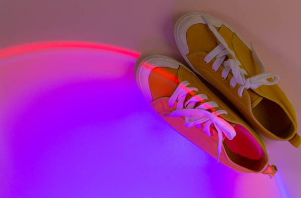 Modne trampki modowe na abstrakcyjnym jasnym tle. Neonowe światła na zwykłych butach. Pomarańczowe i czerwone światło gradientowe. Minimalizm, koncepcja lat 90.. - Zdjęcie, obraz