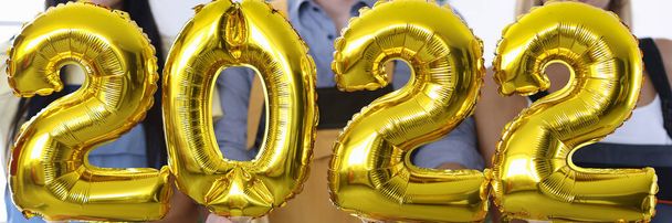 Man and woman builders wearing santa claus hats holding golden balloons with numbers 2022 closeup - Photo, Image