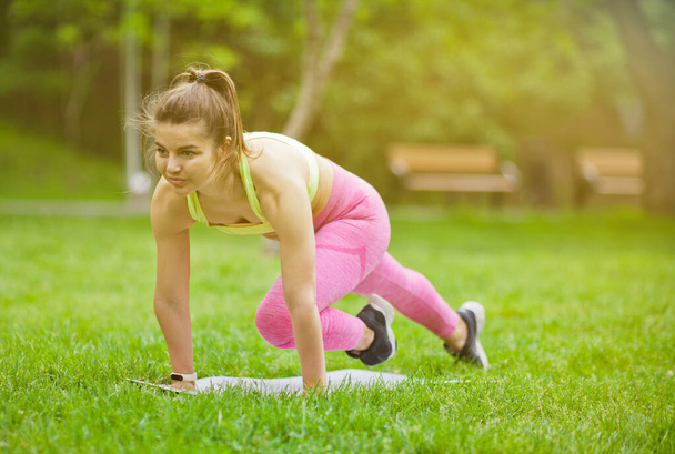 Sportovní fit žena dělá aerobní cvičení na podložce v parku venku - Fotografie, Obrázek
