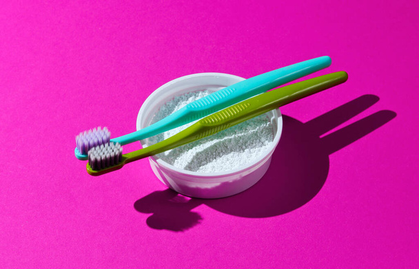 Dwie szczoteczki do zębów, proszek do zębów na różowym neonowym tle. Koncepcja higieny jamy ustnej minimalizmu - Zdjęcie, obraz