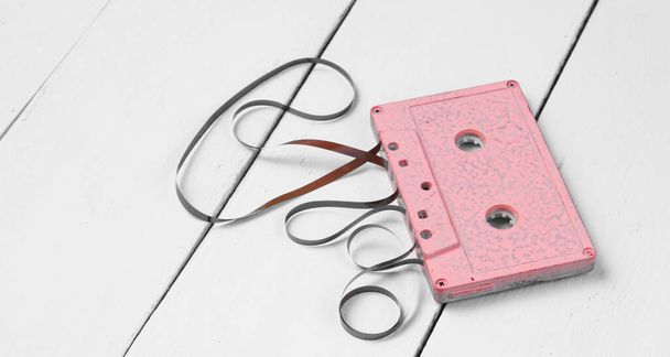 Musikliebhaber Minimalismus Konzept. 80er Jahre im Retro-Stil. Pinkfarbene Audiokassette mit Film auf weißem Holzhintergrund. - Foto, Bild