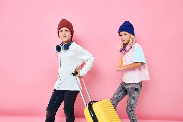 słodkie uśmiechnięte dzieci żółta walizka ze słuchawkami różowy kolor tła - Zdjęcie, obraz