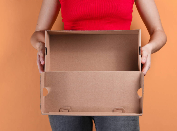 Young woman holding empty cardboard box on orange background. Crop photo, studio shot - Fotó, kép