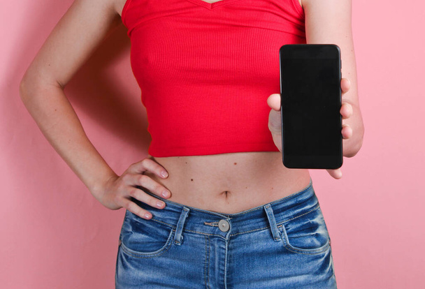 Young woman holds in her hand smartphone on pink background. Crop photo, studio shot - Фото, изображение