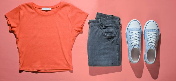 Fashionable orange T-shirt, jeans and sneakers on a pink background. Top view. Flat lay - Fotoğraf, Görsel