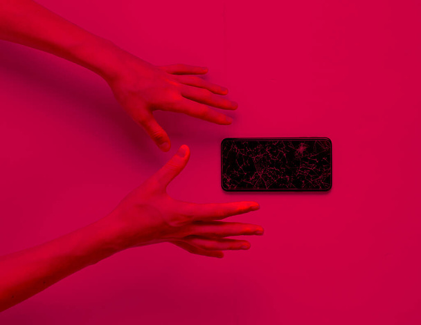 Emotional hands with a broken smartphone. Pink neon light - Fotoğraf, Görsel