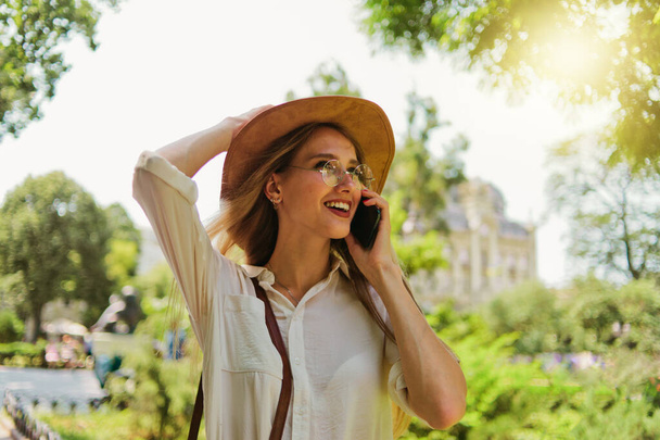 Retrato de una joven rubia de mente única que habla por teléfono y camina por la ciudad al aire libre. - Foto, Imagen