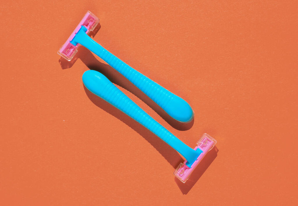 Two blue plastic razors on orange background. Minimalistic beauty and fashion concept - Foto, imagen