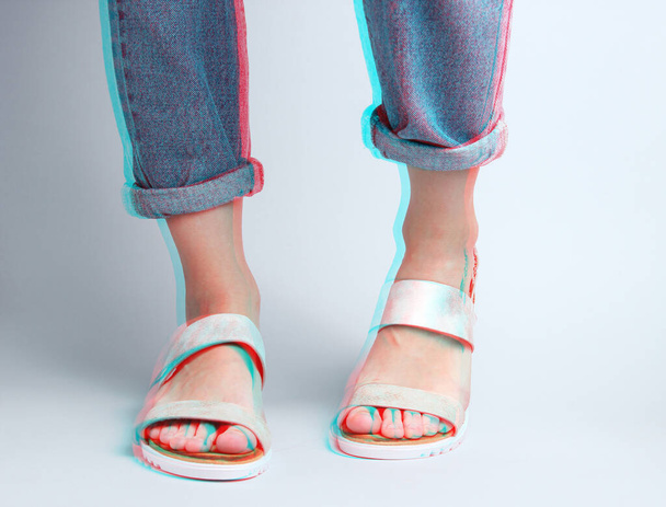 Θραύσμα από γυναικεία πόδια σε μπλε τζιν και μοντέρνα δερμάτινα σανδάλια σε λευκό φόντο. Επιδράσεις λάμψης. Μινιμαλιστικό πλάνο μόδας - Φωτογραφία, εικόνα
