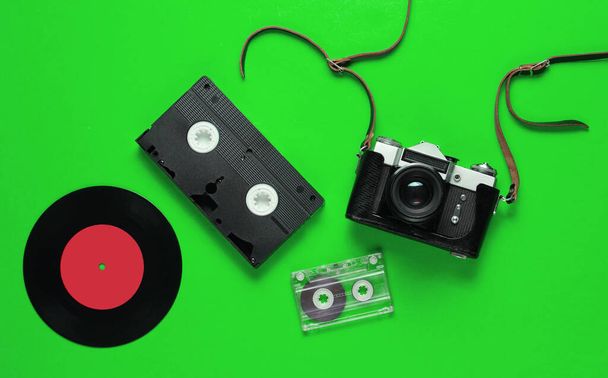 レトロなトップビューはまだ人生。ビニールレコード、ヴィンテージフィルムカメラ、緑の背景にビデオとオーディオカセット。平敷 - 写真・画像