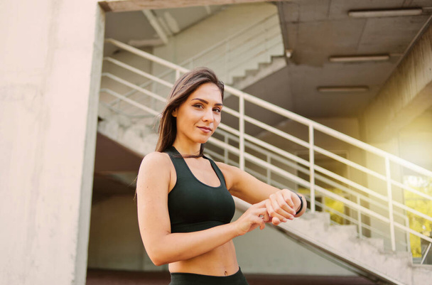 Привлекательная спортивная женщина в спортивной одежде использует умные часы на открытом воздухе в городской среде
 - Фото, изображение