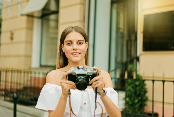 Cheerful blond woman holding retro camera in the urban environment - 写真・画像