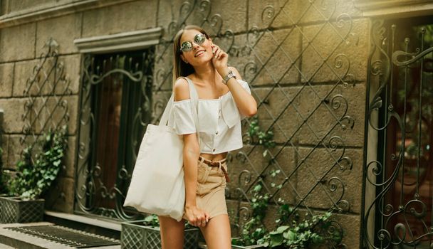 Straatmode. Modieuze stijlvolle vrouw in trendy kleding en zonnebril poseert buiten tegen de achtergrond van oude architectuur - Foto, afbeelding