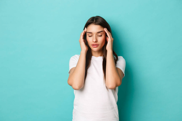 Bild einer jungen attraktiven Frau, die starke Kopfschmerzen hat, den Kopf mit geschlossenen Augen berührt und vor blauem Hintergrund steht - Foto, Bild