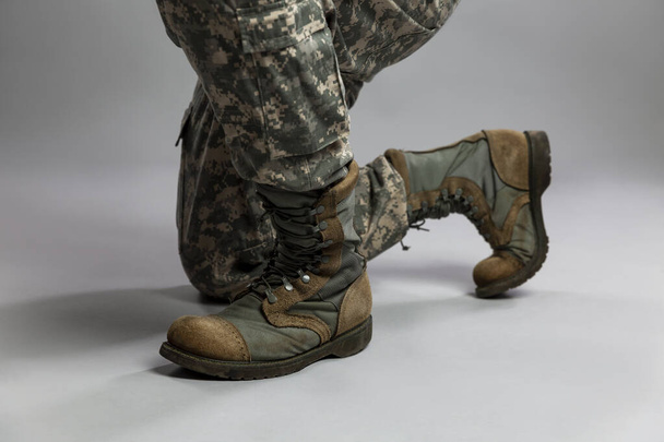 The soldier is on one knee. Legs in camouflage uniforms and US army boots. Memorial Day and military conflicts. Close-up. Gray background. - Фото, изображение