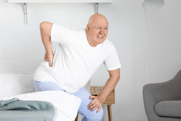 Senior man die last heeft van rugpijn op bed thuis - Foto, afbeelding