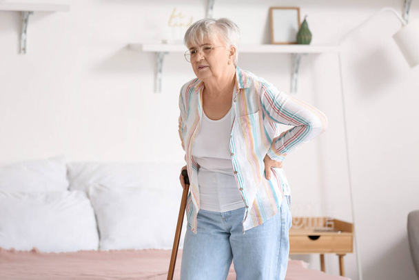 Senior woman with walking stick suffering from back pain in bedroom - Фото, изображение