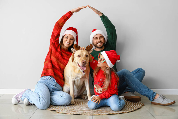Ευτυχισμένη οικογένεια και χαριτωμένο Λαμπραντόρ σκυλί με χριστουγεννιάτικη διακόσμηση κοντά στο φως τοίχο - Φωτογραφία, εικόνα