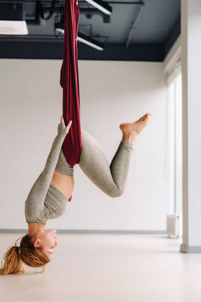 A woman hanging on a hanging hammock does yoga in the gym. - Photo, Image